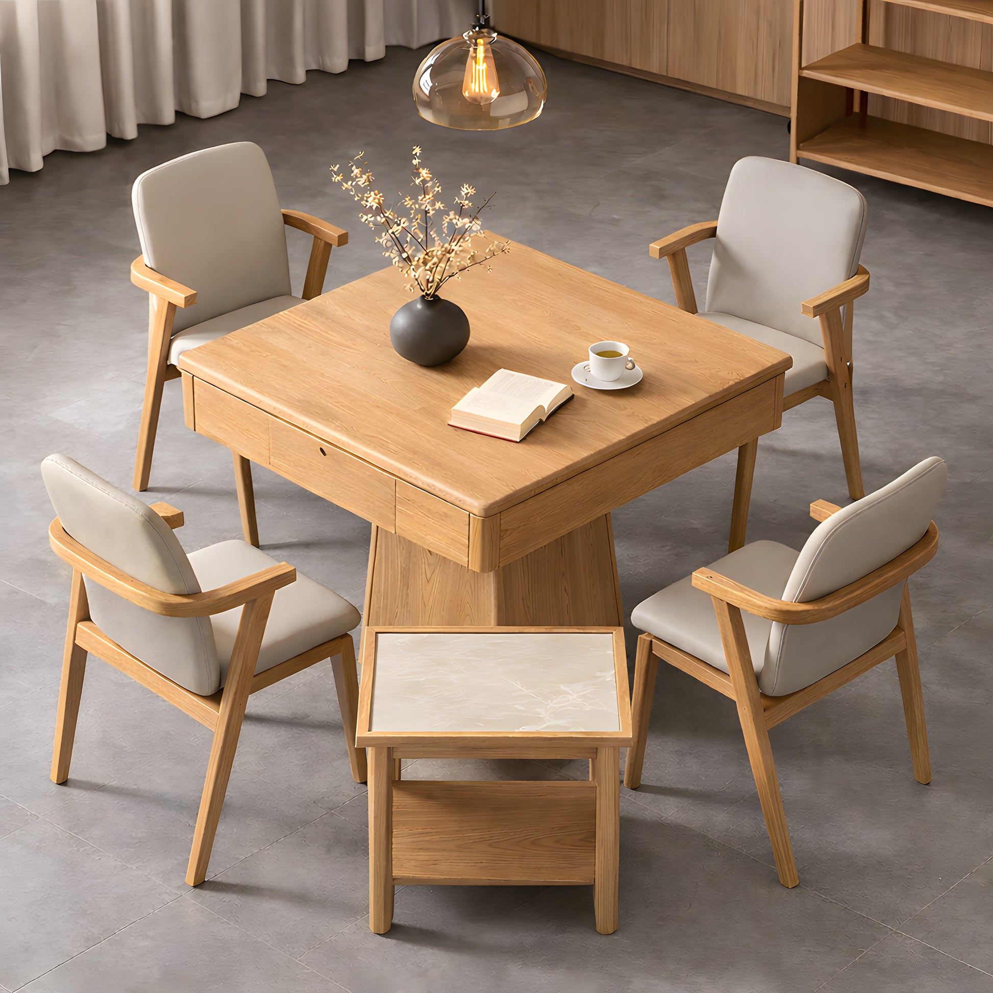 An AUTOJONG automatic mahjong table converted into a stylish dining or work desk with its wooden top cover on. The set includes four beige mid-century modern armchairs and a matching side table with a marble-texture top. Styled with a book, tea cup, and vase under a warm pendant light, showcasing its seamless integration into a modern home interior.