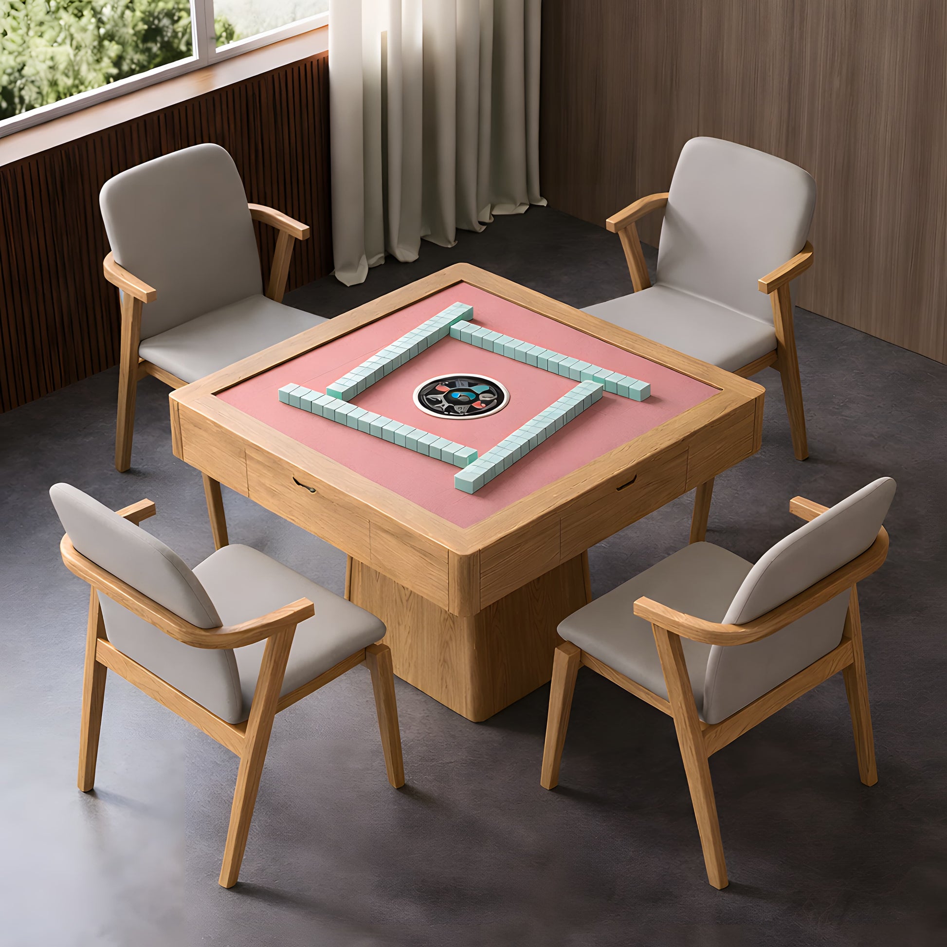 Top-view of an AUTOJONG automatic mahjong table with a premium pink felt surface and four walls of mint green tiles ready for play. The square light-wood table features integrated drawers and is paired with four modern grey upholstered chairs with wooden frames, set in a contemporary room with natural window light.